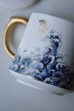 a white and blue coffee cup sitting on top of a table next to a gold ring