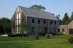 an old barn sits in the middle of a grassy field with trees and bushes around it