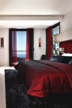 a large bed sitting in a bedroom next to a tall window with red drapes