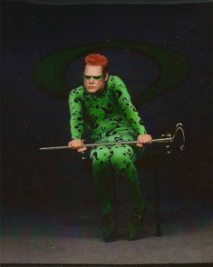 a man dressed in green sitting on a stool with an umbrella behind his back and red hair