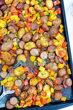 a tray filled with potatoes, peppers and sausages on top of a marble counter