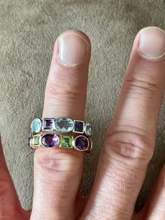 a woman's hand with three different colored stones on it, and one is wearing a gold ring