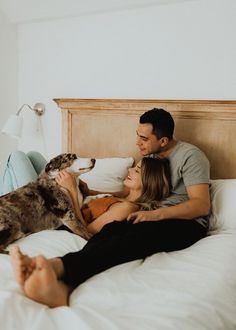 a man and woman laying in bed with their dog