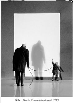 an old man and child are walking in front of a large white wall with a shadow on it