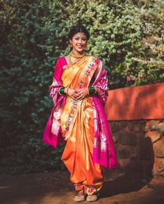 a woman in an orange and pink sari is smiling for the camera with her hands on her hips