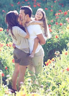 a man and woman kissing while standing in a field full of flowers with their hands around each other