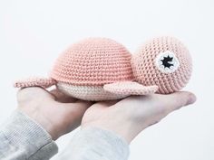 a hand holding two crocheted stuffed animals in their palm, one is pink and the other is white