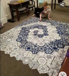 a woman sitting on the floor next to a large blue and white rug with an intricate design