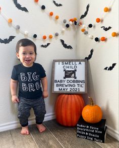 a little boy standing next to a sign with bats on it and a pumpkin in front of him