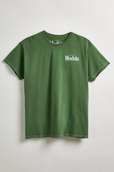 Modelo Cheers graphic tee. Classic cotton jersey tee in a standard fit is topped with Modelo graphics at the left chest and back, ribbed crew neck and short sleeves. Urban Outfitters exclusive. Features Model Cheers graphic tee Front and back graphics Regular fit Ribbed crew neck Short sleeves UO exclusive Content + Care 100% Cotton Machine wash Imported Size + Fit Model is 6’3" and wearing size Medium Measurements taken from size Medium Chest: 24" Length: 26" | Modelo Cheers Tee in Sage, Men's at Urban Outfitters Green Crew Neck T-shirt With Back Print, Urban Outfitters Relaxed Fit T-shirt For Streetwear, Green Relaxed Fit T-shirt With Back Print, Urban Outfitters Cotton Crew Neck T-shirt, Urban Outfitters Casual T-shirt For Streetwear, Casual Urban Outfitters T-shirt For Streetwear, Urban Outfitters Cotton Screen Print T-shirt, Urban Outfitters Cotton T-shirt With Screen Print, Relaxed Fit Graphic T-shirt From Urban Outfitters