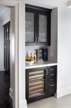 a wine cooler in the corner of a kitchen with black cabinets and marble counter tops