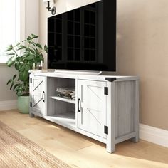 a flat screen tv sitting on top of a white entertainment center next to a potted plant