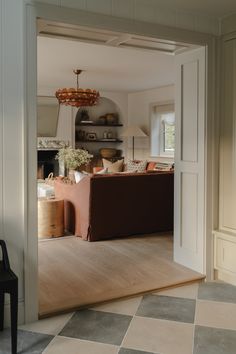 an open door leading to a living room filled with furniture and decor on top of a checkered floor