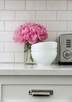 pink flowers are in a white bowl on a counter next to a toaster and microwave