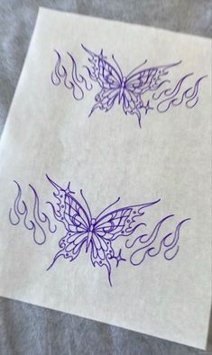 two butterfly tattoos on top of a piece of paper with flames coming out of them