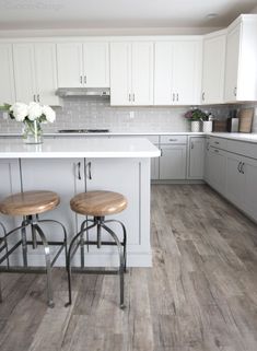 two stools sit at the center of a kitchen island in front of white cabinets