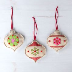 three ornaments hanging from strings on a white surface with red string attached to the ornament