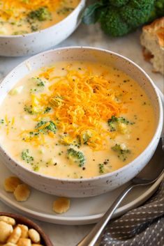 two bowls of broccoli cheese soup with crackers and bread on the side