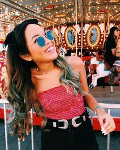 a woman wearing sunglasses standing in front of a merry go round