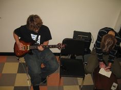 two young men are playing guitars in a room with black and white checkered flooring