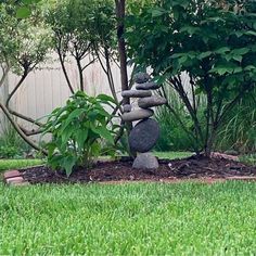 some rocks stacked on top of each other in the middle of a yard with trees and grass