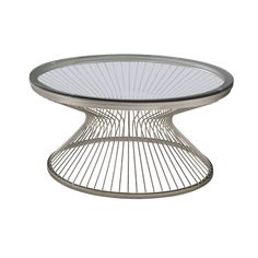 a round glass table with wheels on the bottom and an oval metal base, in front of a white background