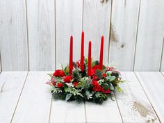 a centerpiece with red candles and greenery in front of a white wooden wall