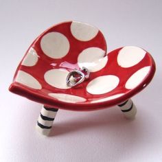 a red and white polka dot heart shaped dish with a ring in it's center