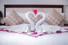 two towels shaped like swans on top of a bed with pink petals in the shape of a heart