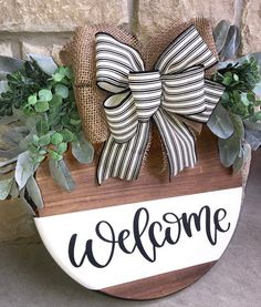 a welcome sign with a bow on it and some greenery in front of a brick wall