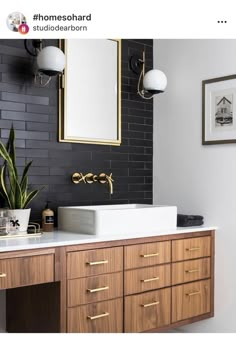 a bathroom with black tiles and gold trim on the vanity, along with a white sink