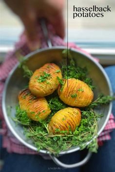 a person holding a metal pan filled with potatoes and green herbs on top of it