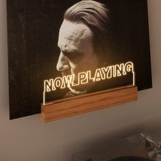 a wooden sign with the words now playing on it and a man's face