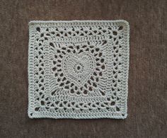 a crocheted square is sitting on the floor in front of a brown carpet