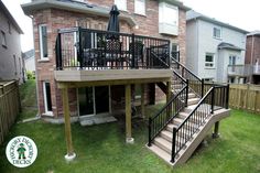 an outdoor deck with stairs and railings in front of a brick house on a sunny day