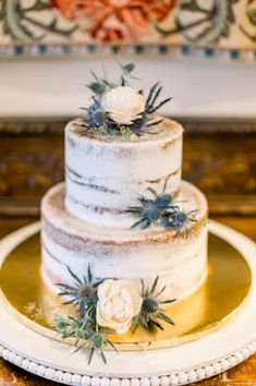 a three tiered cake with white flowers and greenery sits on a gold plate