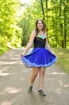 a woman in a blue and black dress is standing on a path with trees behind her