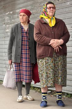 two women standing next to each other in front of a building with a wall behind them