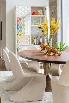 For this dining room, we designed and built our own dining table. We found this gorgeous polished nickel pedestal base and worked with a talented company to create an oval dining table that is 50” wide by 110” long. We are mimicking the proportions of the classic MCM tulip table. This table size completely fills the space and maximizes the seating capacity. On one end of the room we have a fireplace and on the end you can see below, we added a really tall cabinet. The cabinet is white but has a mirrored honeycomb pattern so it reflects the color on the opposite wall. 
We added Panton style chairs in white linen and a custom sized white hair on hide rug. Texture and scale working together here. #midcenturymodern Eclectic Decor Dining Room, Mid Century Modern Dining Room, Custom Coffee Table, Tulip Table, Oval Dining Table, White Dining Room, Tall Cabinet, Rug Texture, Hide Rug