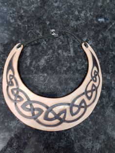 a wooden necklace with an intricate design on the front and back of it, sitting on a marble surface