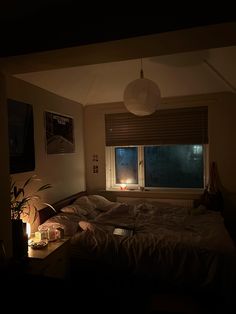 a dimly lit bedroom with the lights on and candles in the window, next to an unmade bed