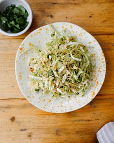 a white plate topped with coleslaw next to a bowl of greens