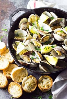 a skillet filled with clams and bread on top of a stone countertop