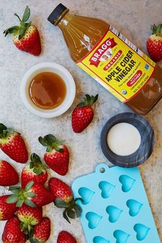 some strawberries and other ingredients are on the counter next to a bottle of syrup