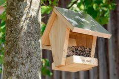 a birdhouse hanging from a tree in the woods with its feeder open for birds to eat