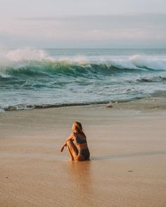 a woman sitting on top of a sandy beach next to the ocean with waves coming in