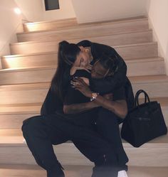 a man and woman hugging on the steps in front of some stairs with a handbag