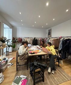 two people sitting at a table in a clothing store with clothes hanging on the walls