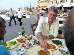 three people sitting at a table with plates of food in front of them on the street