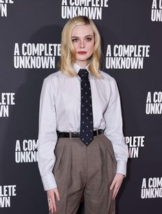 a woman in a tie and dress shirt posing for the camera on a red carpet